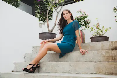 young stylish beautiful woman blue dress summer fashion trend vacation garden tropical hotel terrace smiling sitting stairs long legs shoes heels